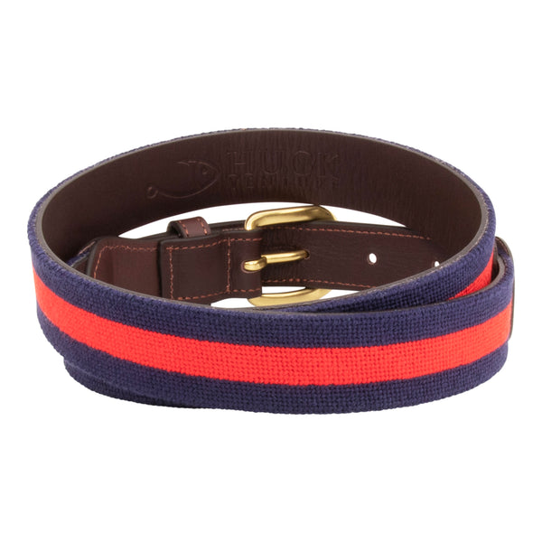 Navy Stripe Needlepoint Belt with a dark navy blue background showing a red stripe 1/3 the width of the belt going down the center of the belt. Belt has a brass buckle and full grain leather backing and strap.