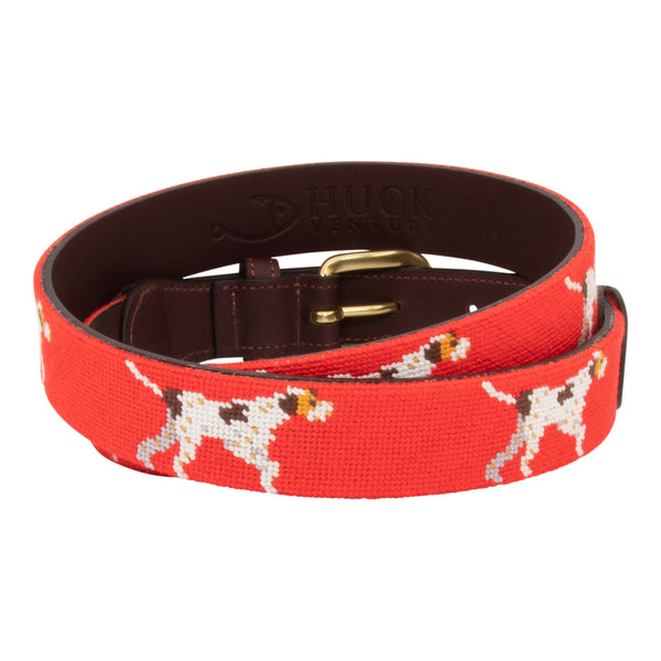 Pointer Dog Needlepoint Belt with a blaze orange background showing a repeating pattern of evenly spaced upland hunting dogs in a pointing stance. The belt has a brass buckle and full grain leather backing and strap.