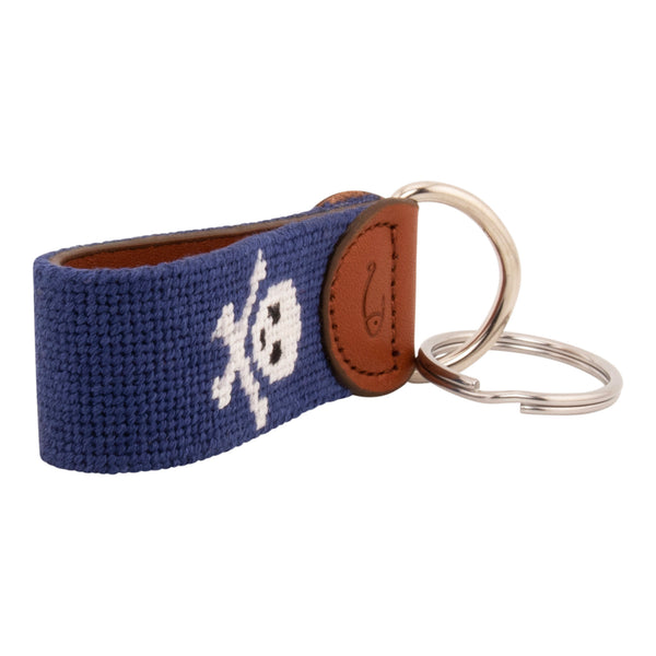 needlepoint key fob with white jolly rogers skull and crossbones against a dark navy blue background, same image on both sides, hand-stitched, leather backing, stainless steel keyring