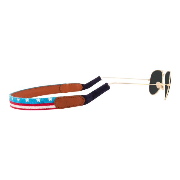 American Flag  banner needlepoint sunglass strap showing the American Flag in banner format across the whole sunglass strap.  The strap has a sturdy cotton covered silicone ear connectors and a soft leather backing